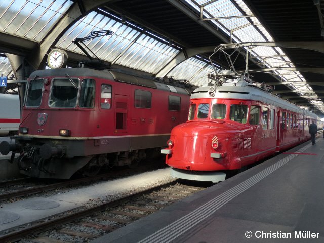 Vom Sonnenlicht erhellt steht am Hauptbahnhof in Zürich ein roter Doppelpfeil (Churchill-Pfeil) neben der Elektrolok 11247 zur Abfahrt bereit. Die Aufnahme entstand am So, den 10.4.2016.