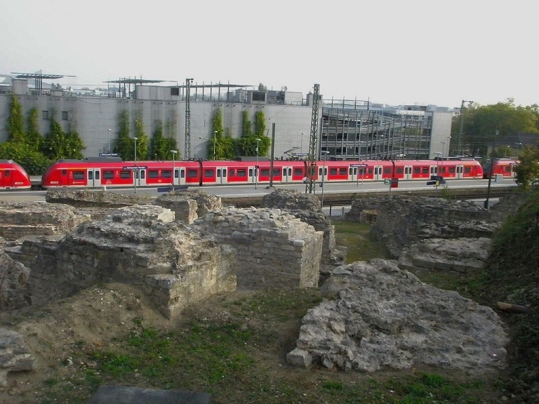 Der dreiteilige S-Bahn-Zug hÃ¤lt an der Haltestelle Mainz, RÃ¶misches Theater. Im Vordergrund stehen die Fundamentreste eines antiken Theaters. Direkt neben dem Bahnhof sind diese Ausgrabungen zu sehen. Sozusagen ein S-Bahn-Halt mit Museums-Charakter. 