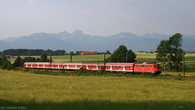 Eine Bügelfaltenlok der Reihe 110 hat am Morgen des 14.07.2009 einen Pendlerzug von Kufstein nach München am Haken. Zwischen Großkarolinenfeld und Ostermünchen wurde das Ganze samt Alpen im Hintergrund aufgenommen.
