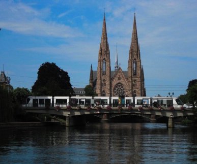 Eine Straßenbahn der neuesten Generation, eine Citadis-Straßenbahn vom Hersteller Alstom, hält an der Haltestelle Gallia auf der Pont Royal in Strasbourg. Im Hintergrund ist die Fassade der Paulskirche zu sehen. Die Aufnahme ist von Juli 2019.